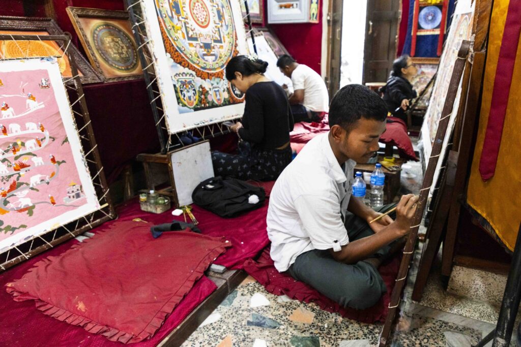 Pasang Ghising sits on the floor of the painting school while painting with classmates. 